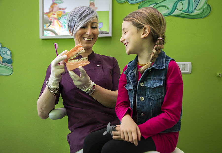 Dentista pediatrica di Ferman For Kids interagisce sorridendo con una bambina nella sala visite colorata, mostrando un approccio giocoso e rassicurante
